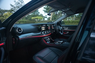 The image depicts the interior of a luxury car, featuring a sleek, modern dashboard with illuminated displays and ambient lighting. The black leather seats complement the high-tech controls and touchscreen interface.