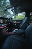 The interior of a luxury car features modern black leather seats and a sleek dashboard with illuminated controls. The ambient lighting along the dashboard adds an elegant touch, while the outside view through the windows reveals a green, leafy landscape.