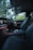 The interior of a luxury car features modern black leather seats and a sleek dashboard with illuminated controls. The ambient lighting along the dashboard adds an elegant touch, while the outside view through the windows reveals a green, leafy landscape.