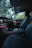 The interior of a luxury car features modern black leather seats and a sleek dashboard with illuminated controls. The ambient lighting along the dashboard adds an elegant touch, while the outside view through the windows reveals a green, leafy landscape.