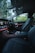 The interior of a luxury car features modern black leather seats and a sleek dashboard with illuminated controls. The ambient lighting along the dashboard adds an elegant touch, while the outside view through the windows reveals a green, leafy landscape.