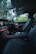 The interior of a luxury car features modern black leather seats and a sleek dashboard with illuminated controls. The ambient lighting along the dashboard adds an elegant touch, while the outside view through the windows reveals a green, leafy landscape.