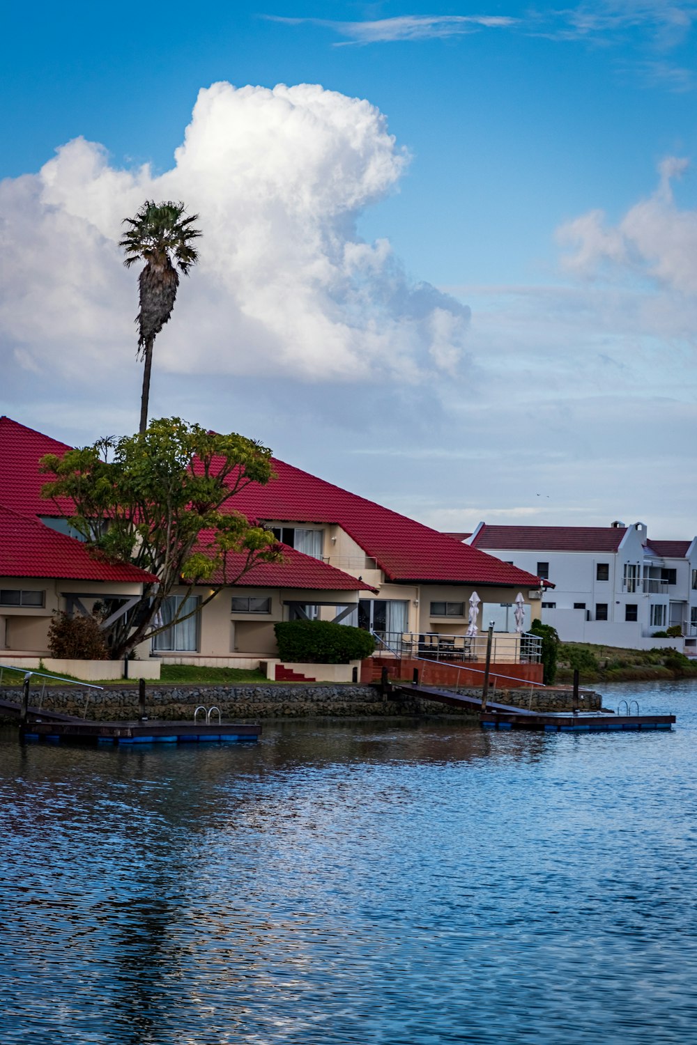 white and red concrete house beside body of water under white clouds during daytime