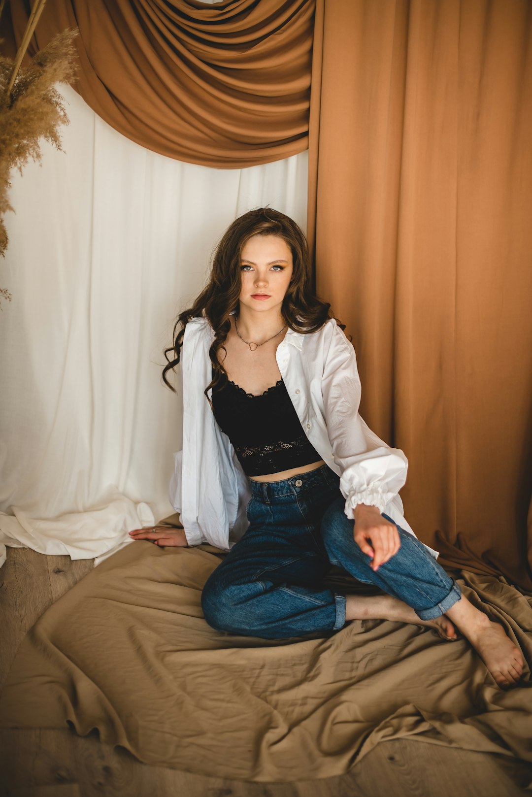 woman in white cardigan and blue denim jeans sitting on brown bed