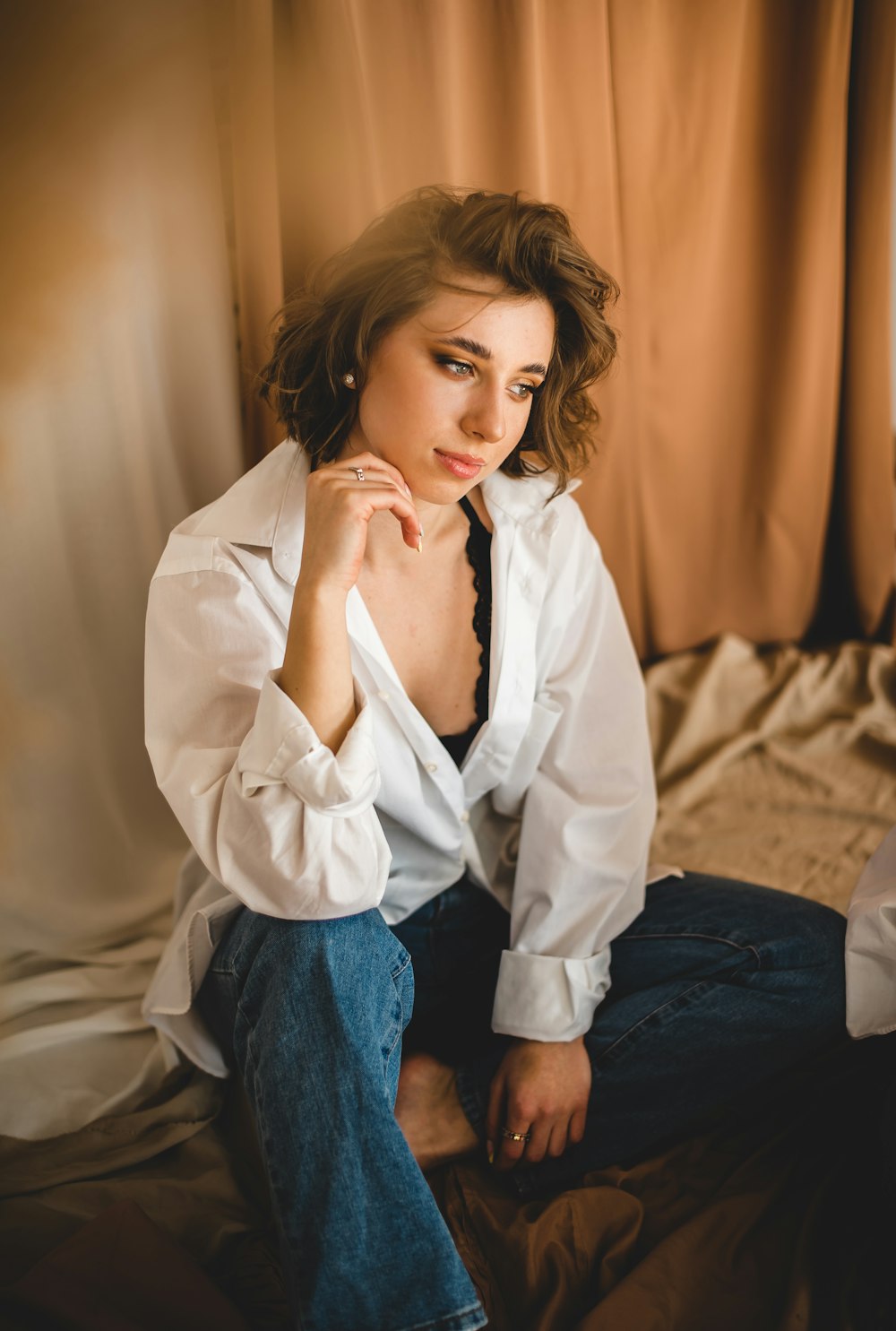 woman in white button up long sleeve shirt and blue denim jeans sitting on white bed