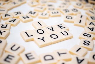 Scrabble-style letter tiles are arranged on a surface to spell out 'I LOVE YOU', surrounded by more scattered tiles with random letters.