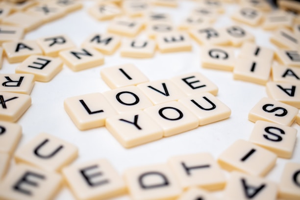 Scrabble-style letter tiles are arranged on a surface to spell out 'I LOVE YOU', surrounded by more scattered tiles with random letters.