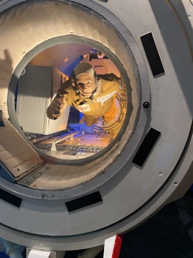 A mannequin in an astronaut suit labeled 'Stafford' is positioned inside a space module. The scene is well-lit, highlighting the orange suit and intricate details of the module's interior, which features various panels and controls.