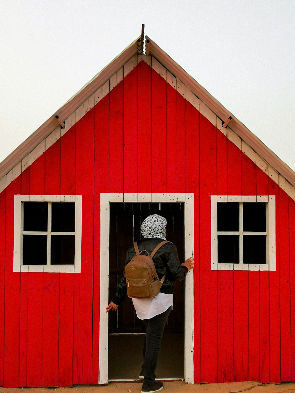 woman in brown jacket standing in front of red wooden barn
