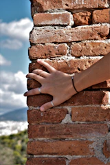 Hand wearing stackable rings with geometric shapes against a muted city backdrop.