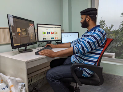 An Indian professional working at a desk with multiple screens showing accounts and taxation data.
