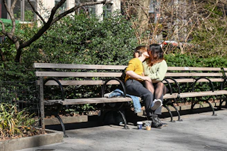 A couple sitting close together on a park bench, gently holding hands and sharing a quiet moment.