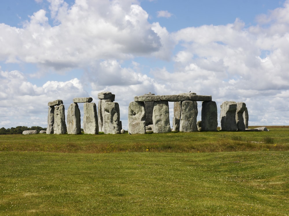 gray rock formation on green grass field under white clouds during daytime