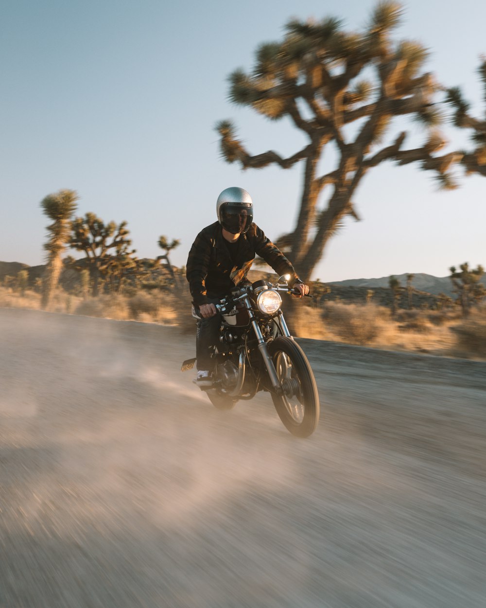 昼間の道路でバイクに乗る黒いジャケットの男