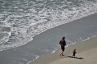 Father and daughter walking along a beach, their footprints trailing behind them in the sand.