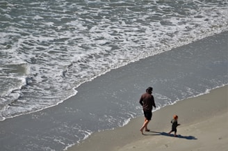 Father and daughter walking along a beach, their footprints trailing behind them in the sand.