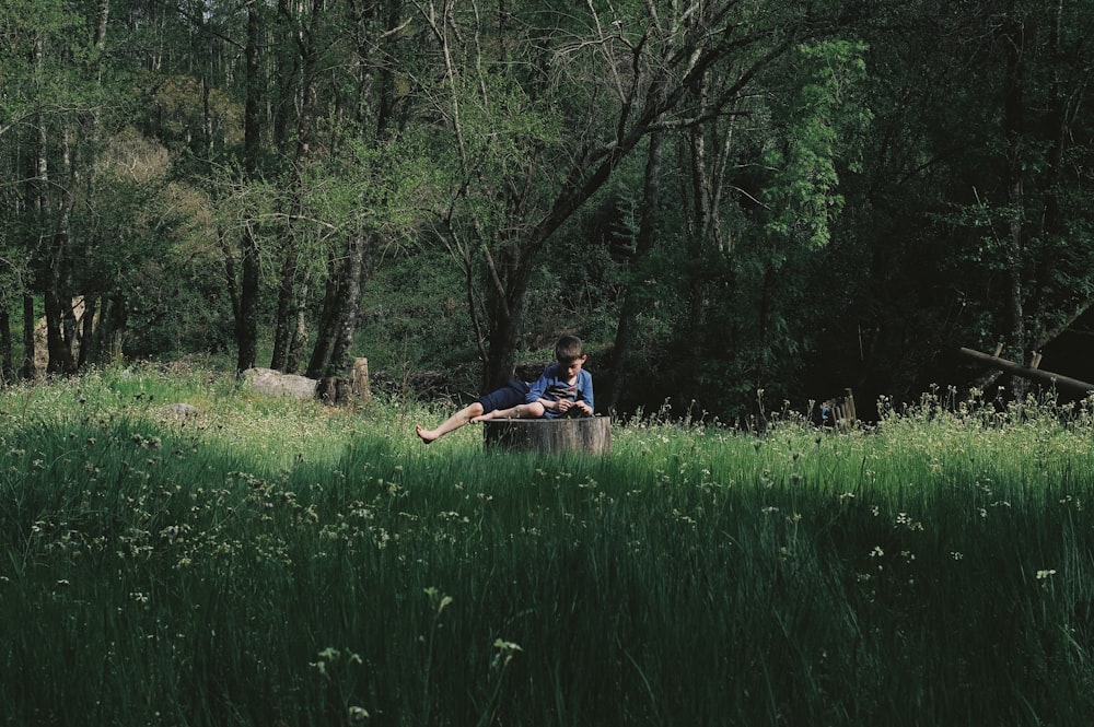 man in blue shirt sitting on brown wooden boat on green grass field during daytime