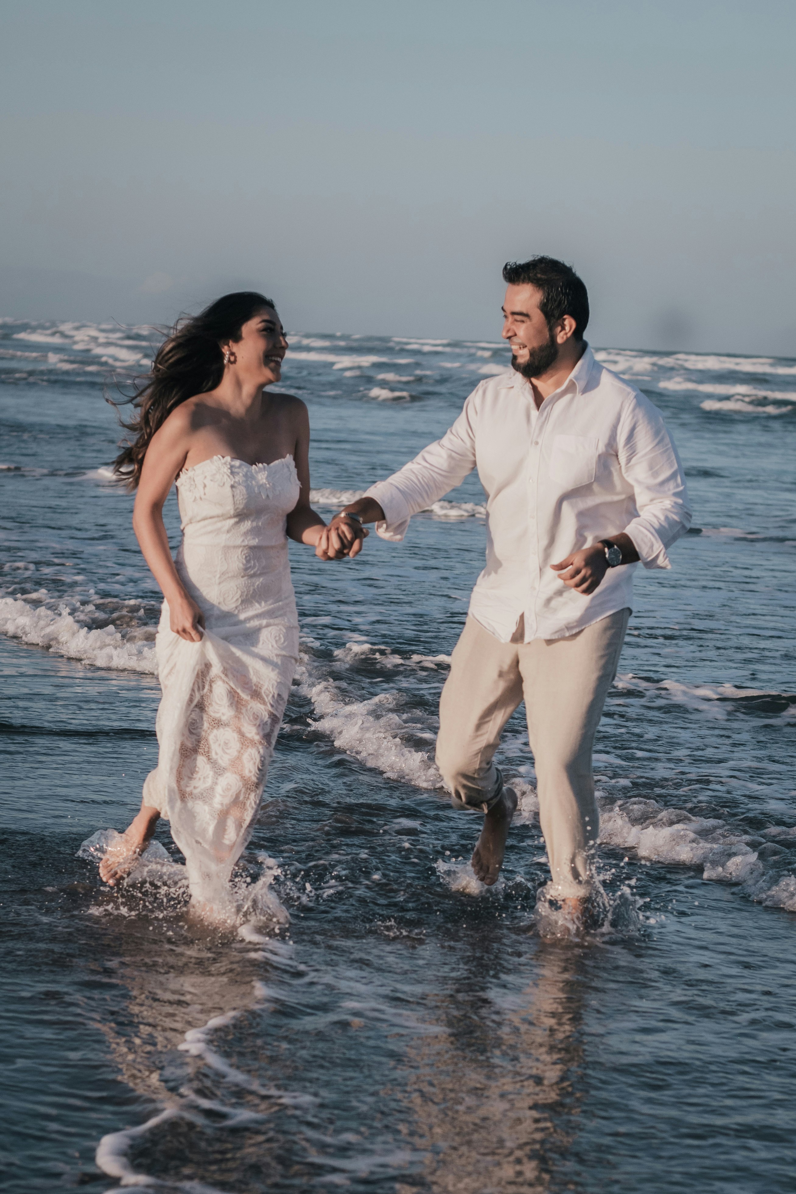 man and woman in white dress walking on sea shore during daytime