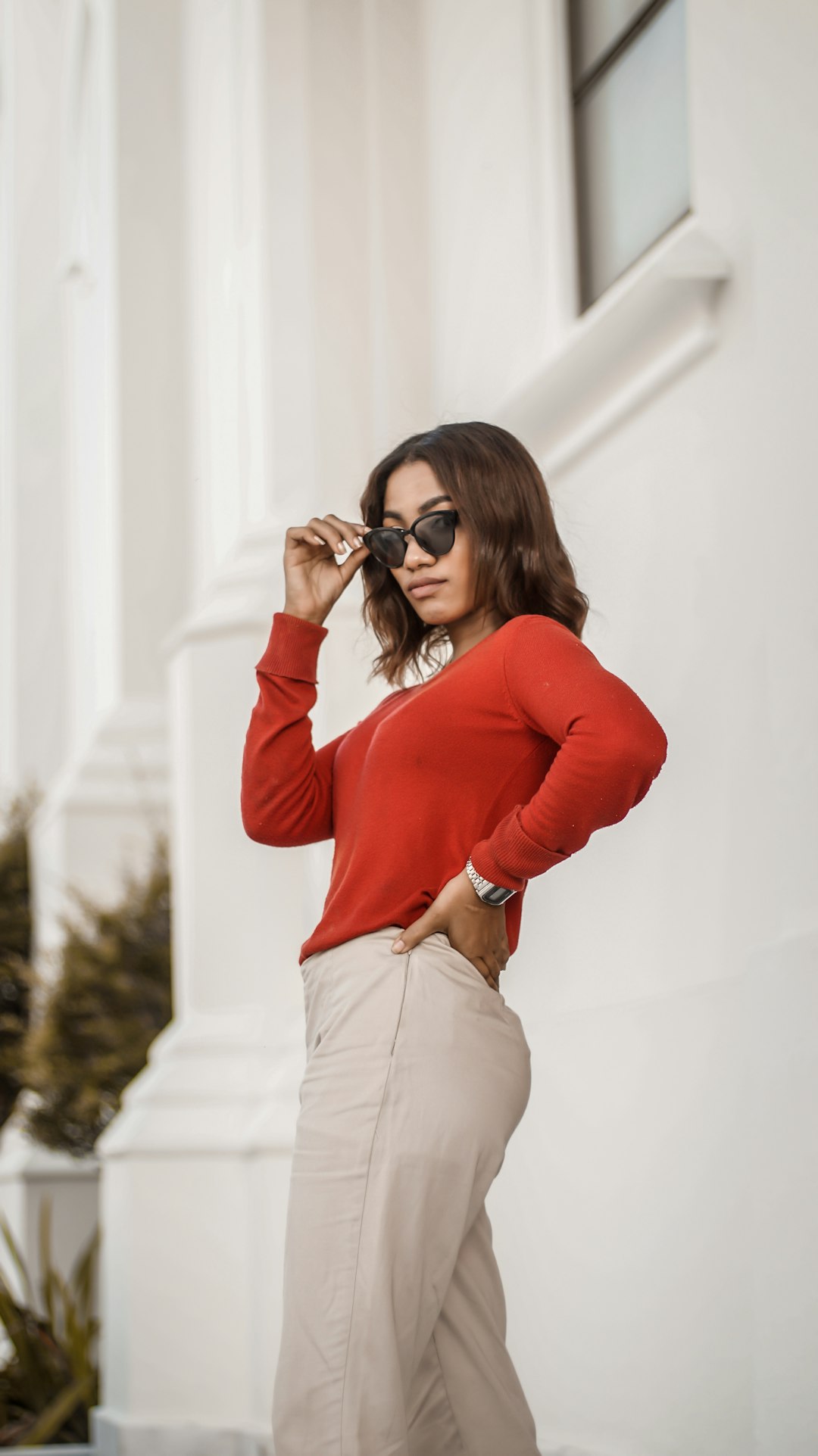 woman in red long sleeve shirt and beige pants wearing black sunglasses