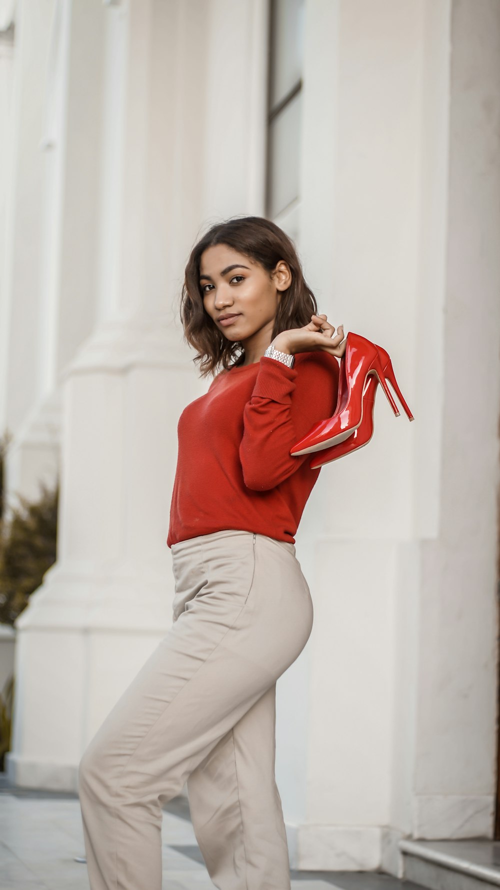 woman in red long sleeve shirt and white pants holding red leather handbag