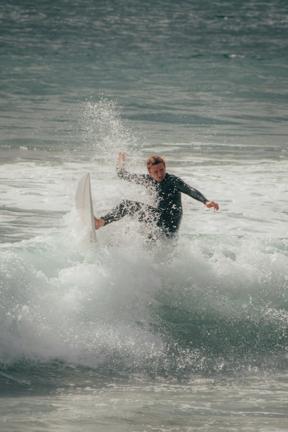 昼間、海の波でサーフィンをする黒いウェットスーツを着た男