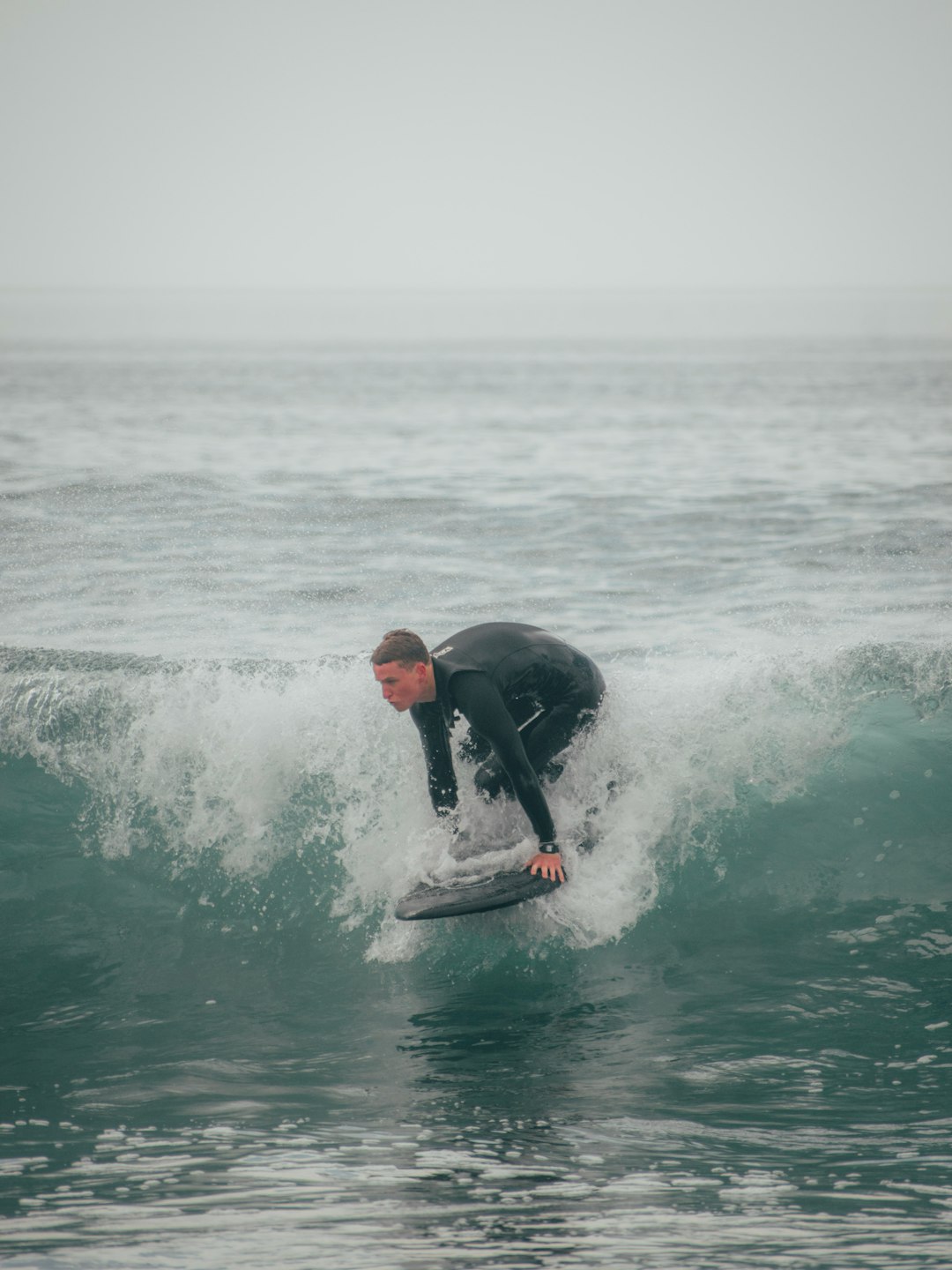 man in black wet suit surfing on sea waves during daytime