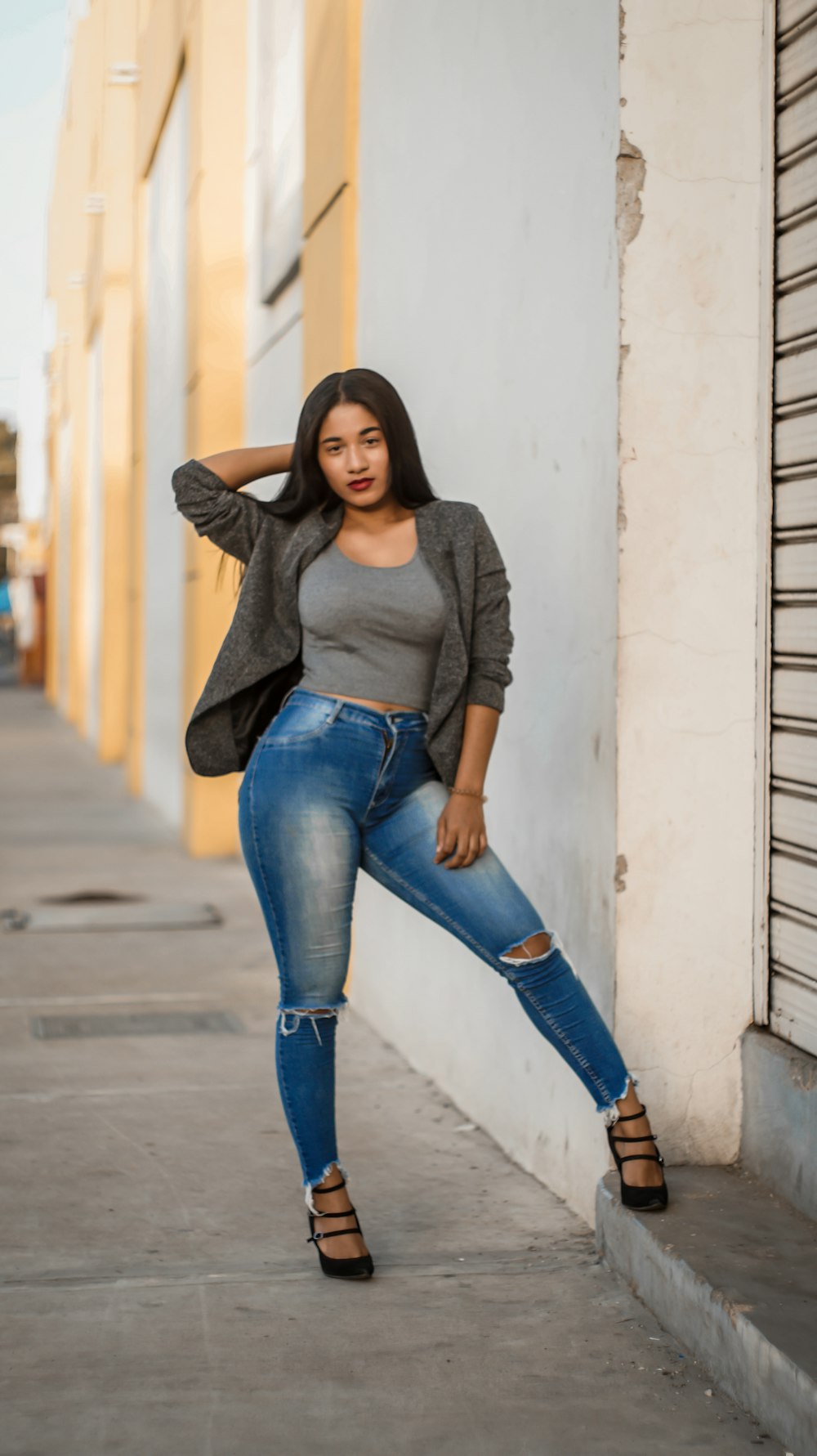 woman in black long sleeve shirt and blue denim jeans leaning on white wall during daytime