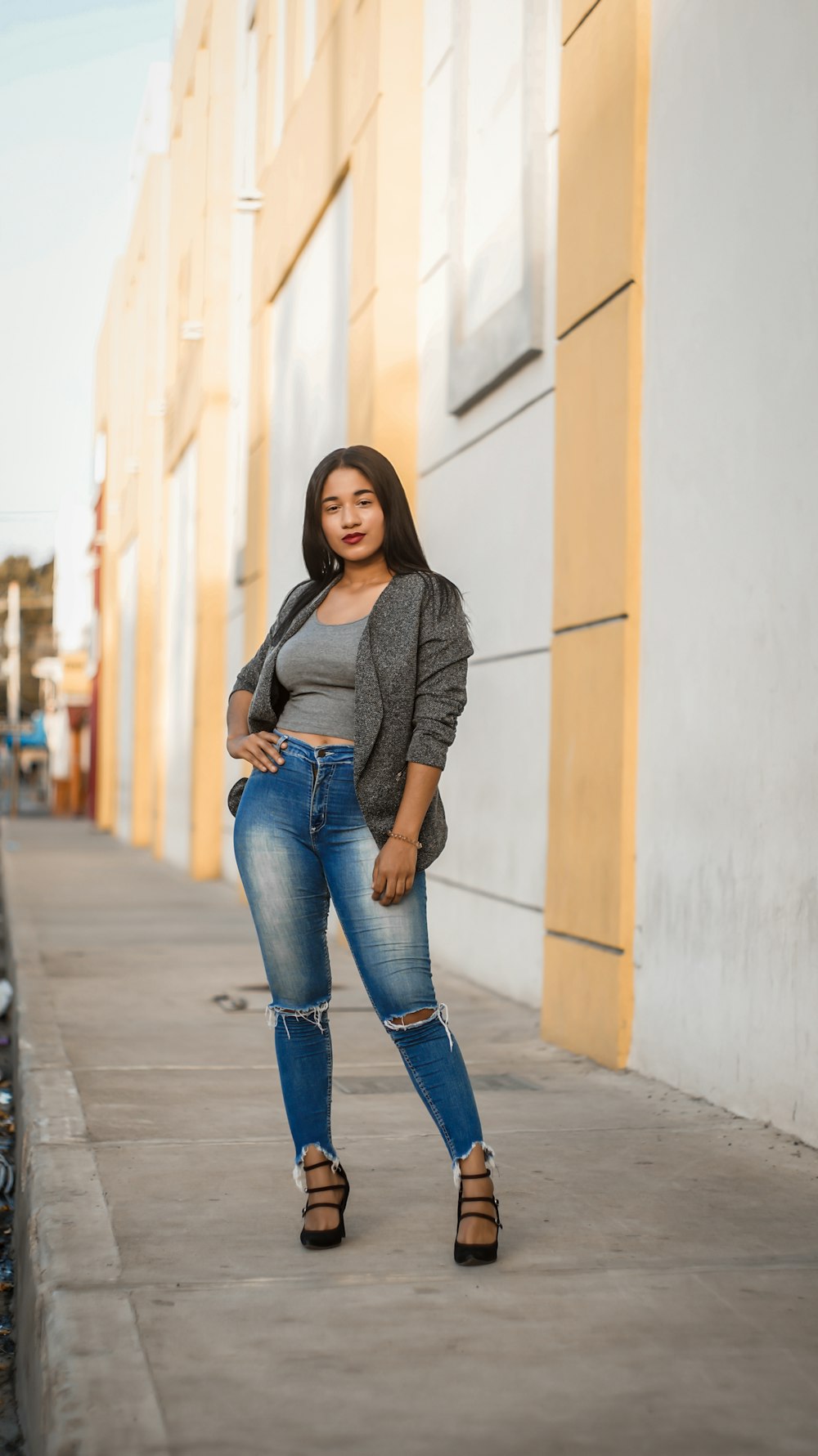 woman in gray long sleeve shirt and blue denim jeans standing on sidewalk during daytime