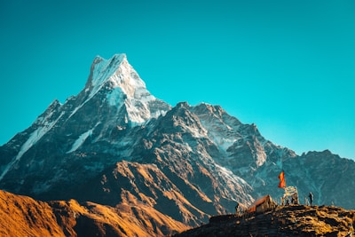 person in orange jacket standing on brown rock near snow covered mountain during daytime
