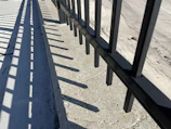 A close-up of a metal fence with geometric patterns casting shadows on a stone pathway.