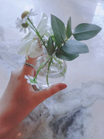 A close-up of a hand holding a textured, bright stoneware vase filled with fresh wildflowers.