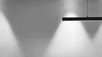 Minimalist diamond-shaped light fixture casting subtle silver highlights over a clean, dark workspace.