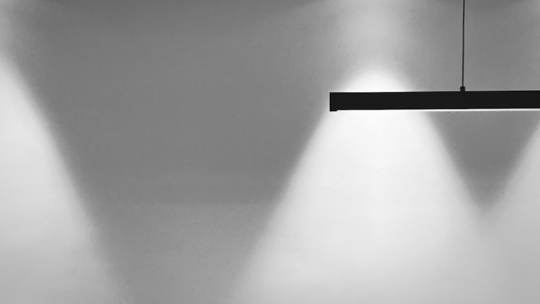 A minimalist light fixture glowing gently against a light black wall.