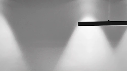Minimalist diamond-shaped light fixture casting subtle silver highlights over a clean, dark workspace.