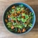 A bowl filled with a quinoa salad featuring roasted sweet potato chunks, fresh greens, black beans, chopped red onions, and drizzled with a green dressing.
