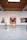 An art gallery with white walls displays three large, colorful paintings. A person wearing a white dress and neon green shoes stands in the middle of the room. The gallery has an industrial style ceiling with exposed wooden beams and spotlights.