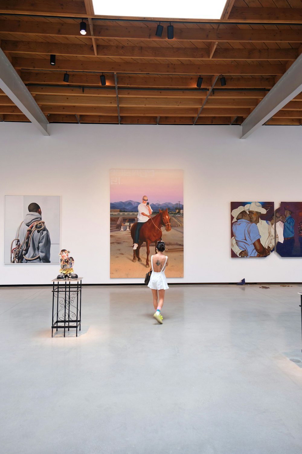 woman in white tank top and black skirt standing in front of wall with paintings