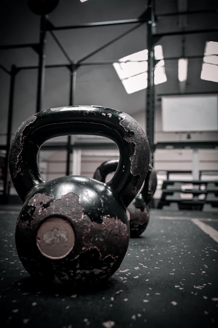 Close-up of a hand gripping a heavy kettlebell with a splash of chalk dust in a lively CrossFit gym