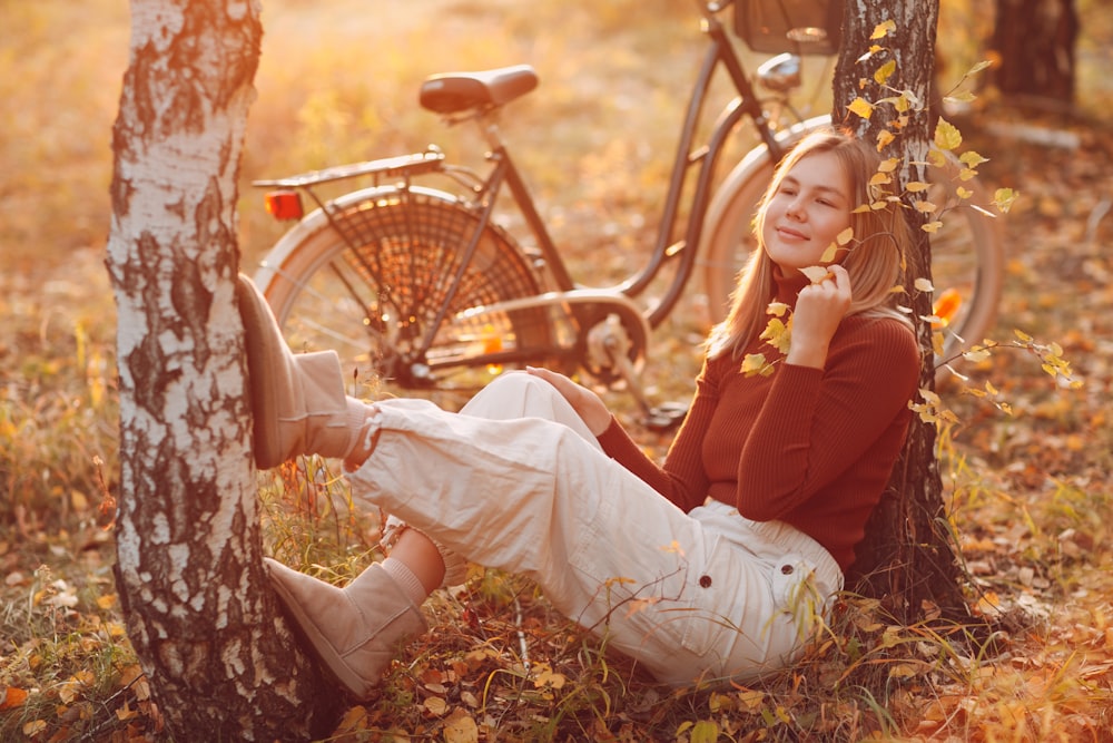 Donna in camicia marrone a maniche lunghe e pantaloni bianchi seduti su foglie secche marroni
