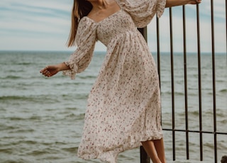 woman in white and red floral dress standing on brown wooden fence during daytime