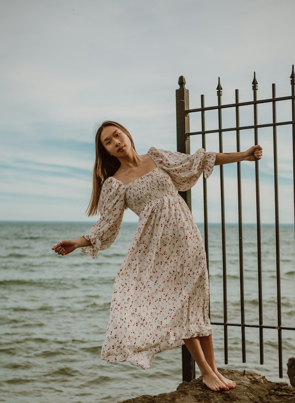 woman in white and red floral dress standing on brown wooden fence during daytime