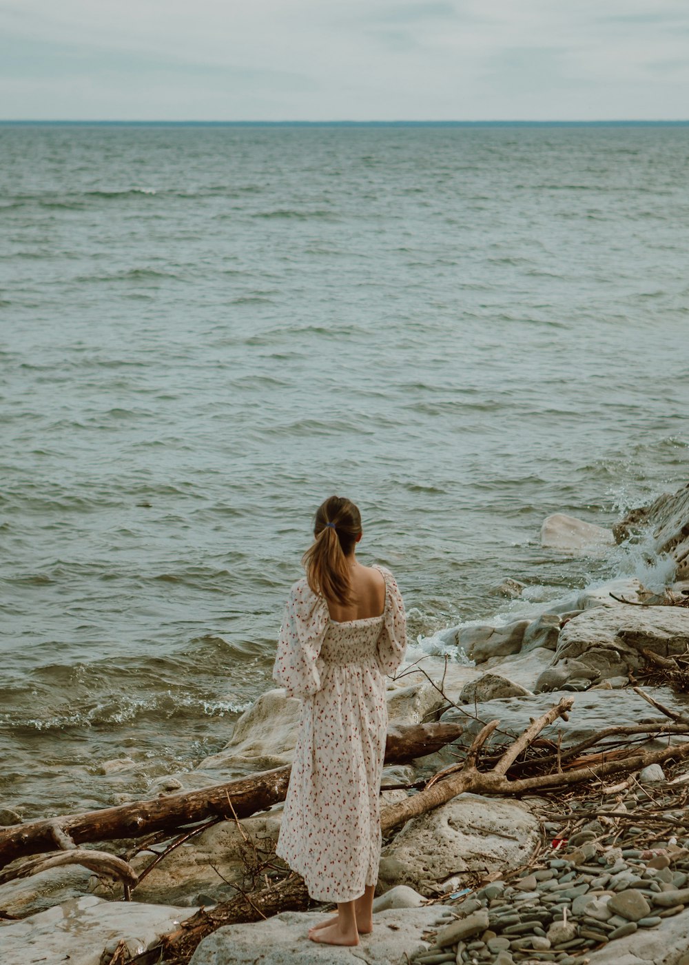 woman in white dress sitting on brown wood log on beach during daytime