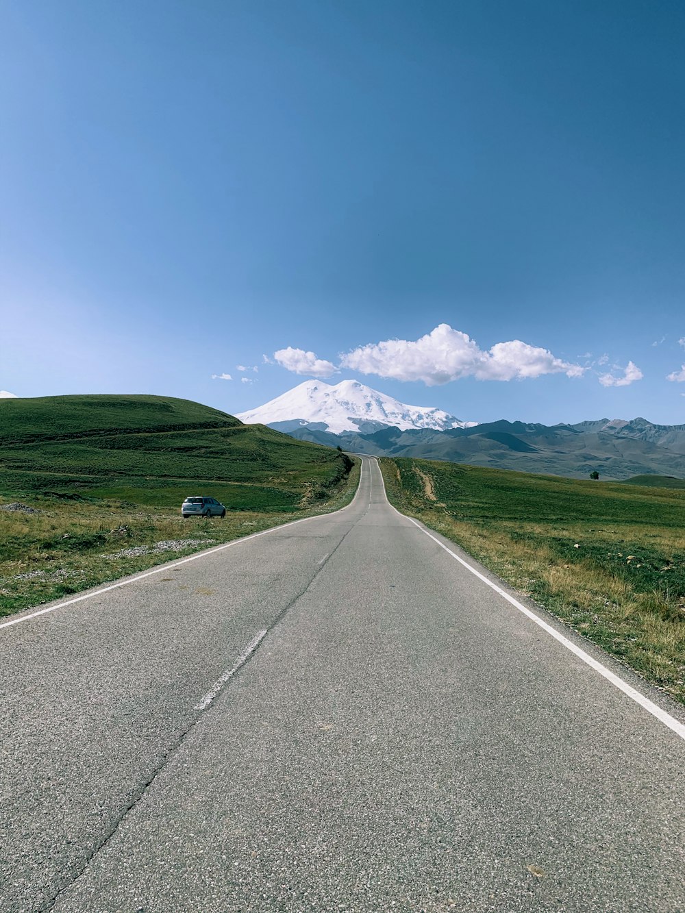 gray concrete road between green grass field under blue sky during daytime