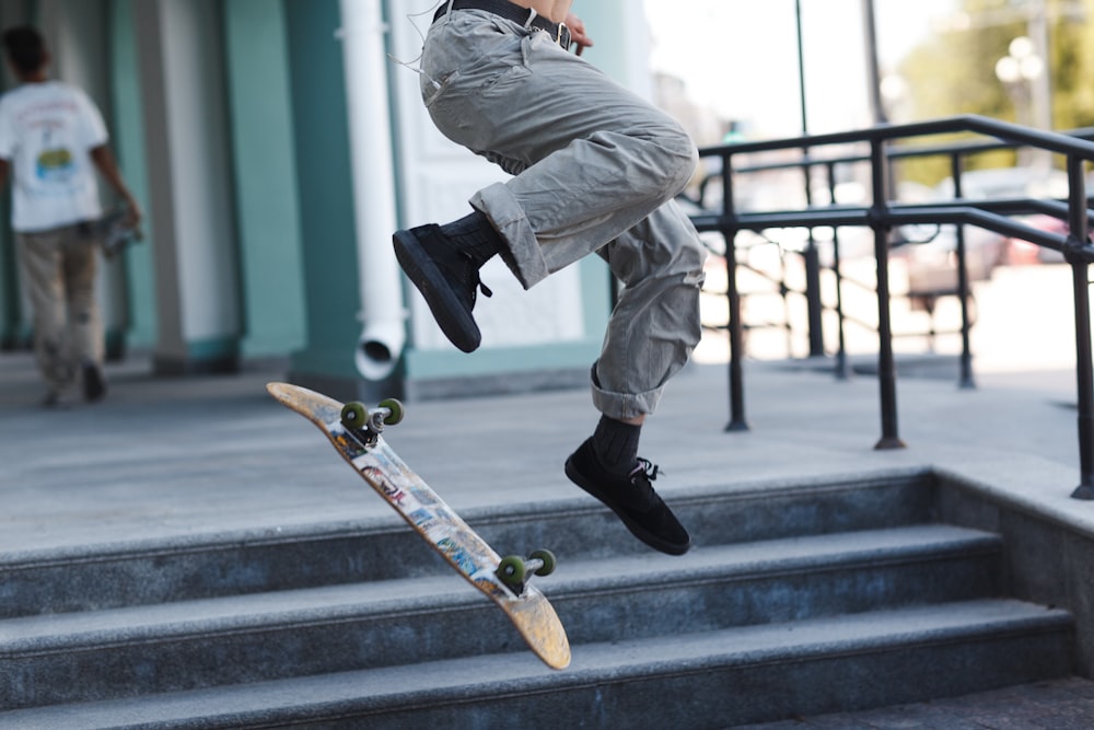 uomo in pantaloni grigi e scarpe nere che cavalcano lo skateboard