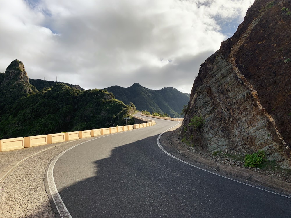 Route en béton gris entre la montagne brune sous les nuages blancs pendant la journée