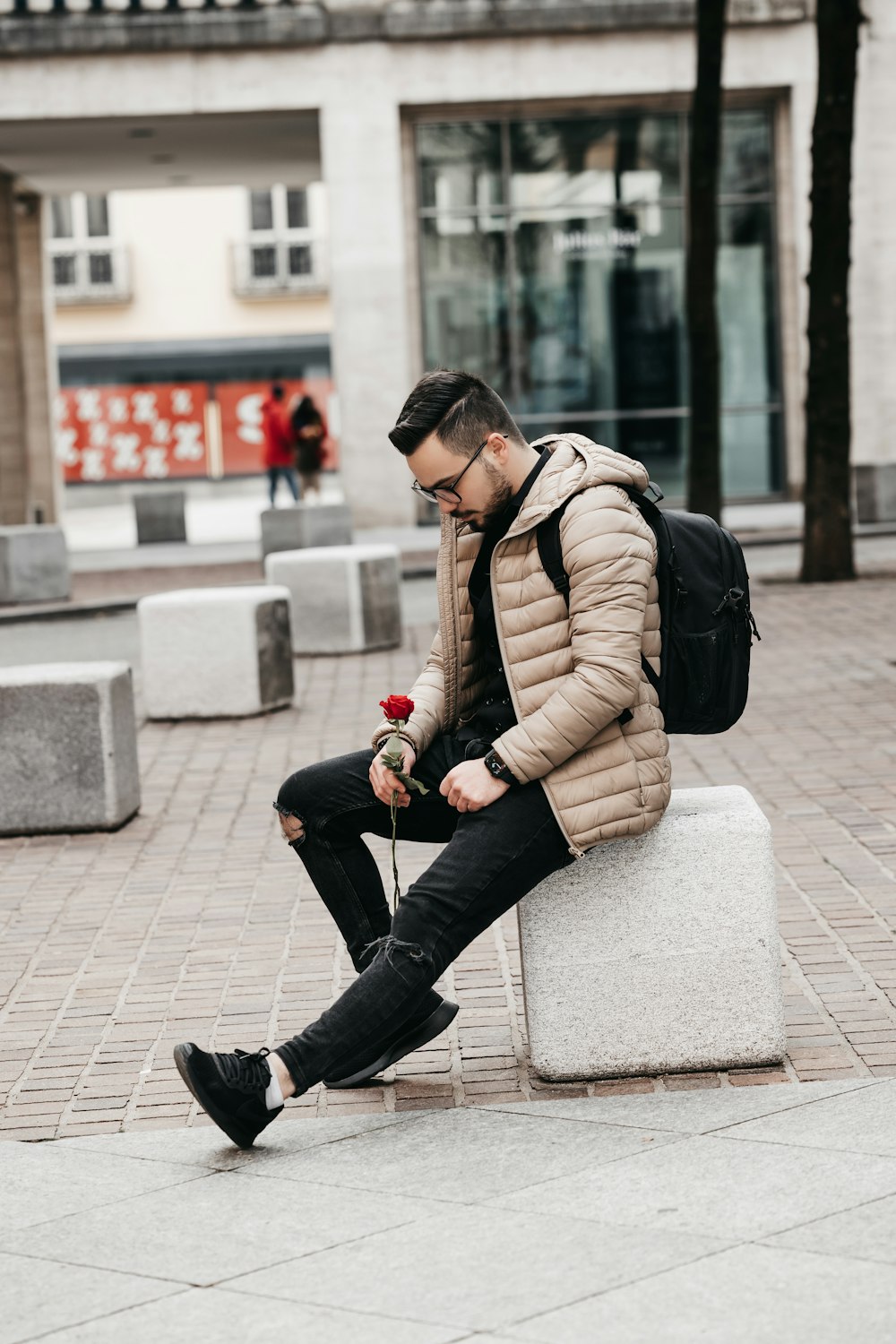 woman in brown jacket and black pants sitting on concrete bench during daytime