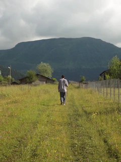 man in gray jacket walking on green grass field during daytime