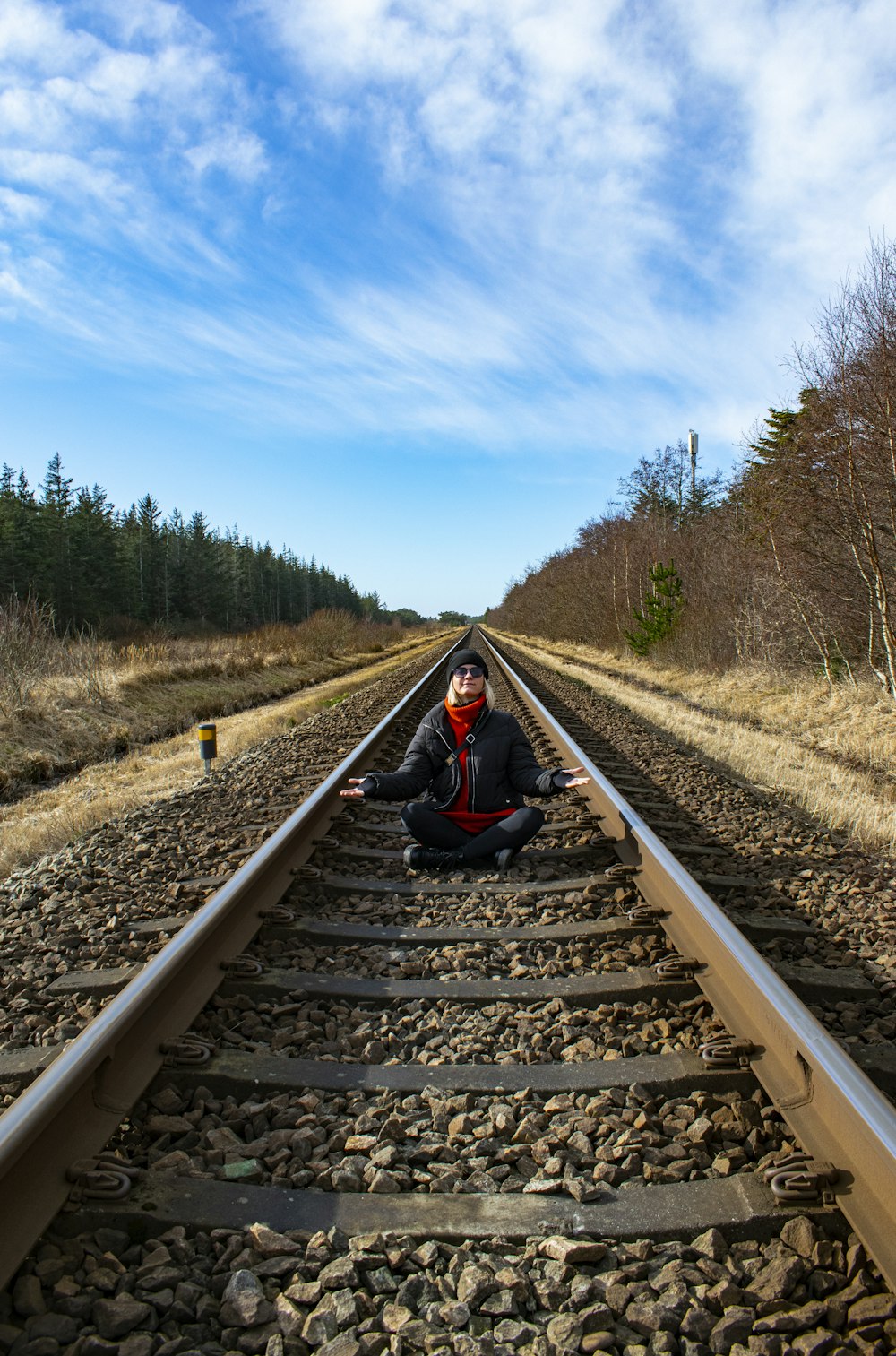 person in black jacket sitting on train rail during daytime