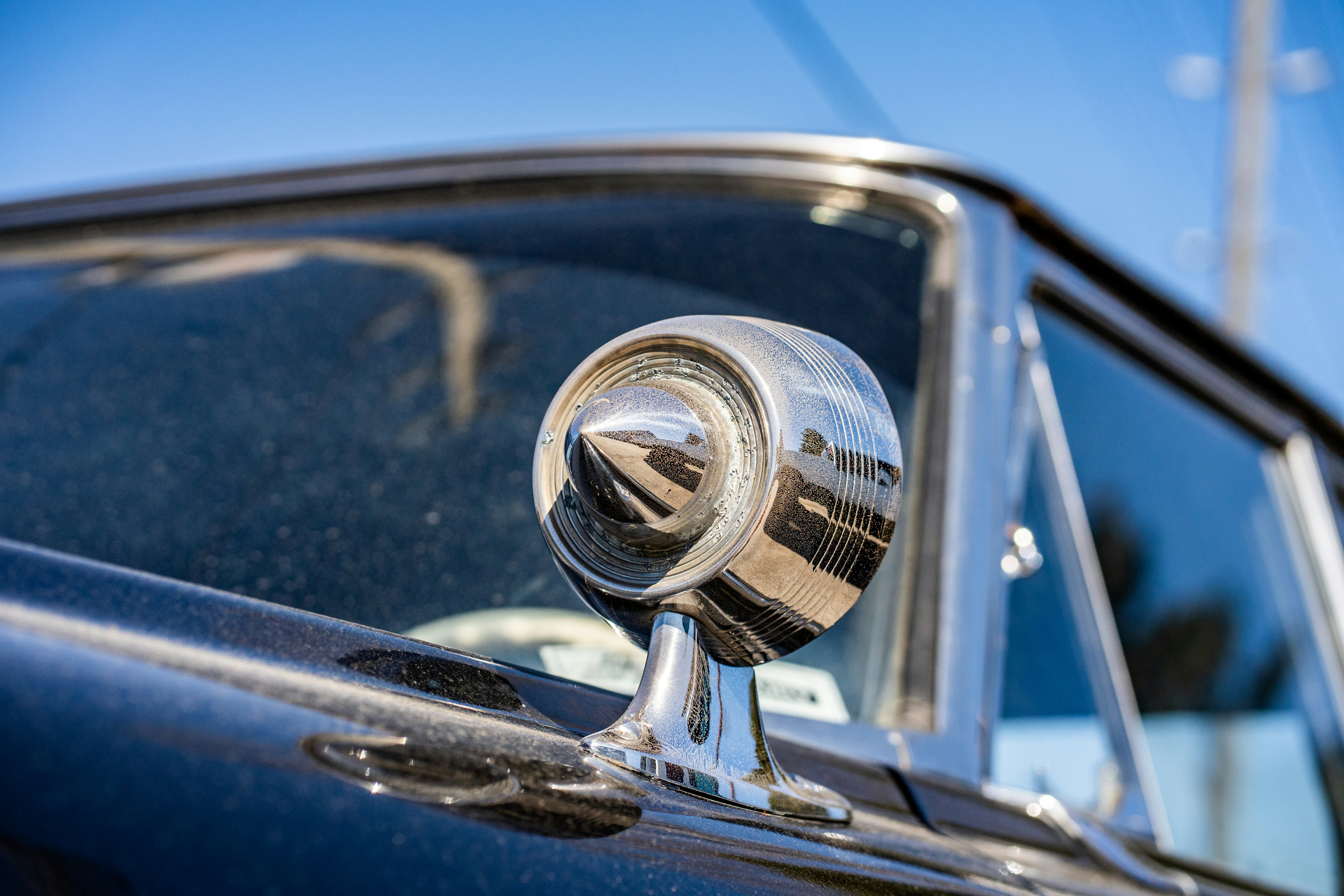 Classic Beetle side mirror with a polished metal finish against a bright blue sky.