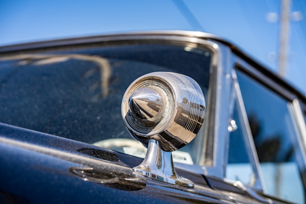 Shiny chrome side mirrors reflecting a clear blue sky on a classic car.
